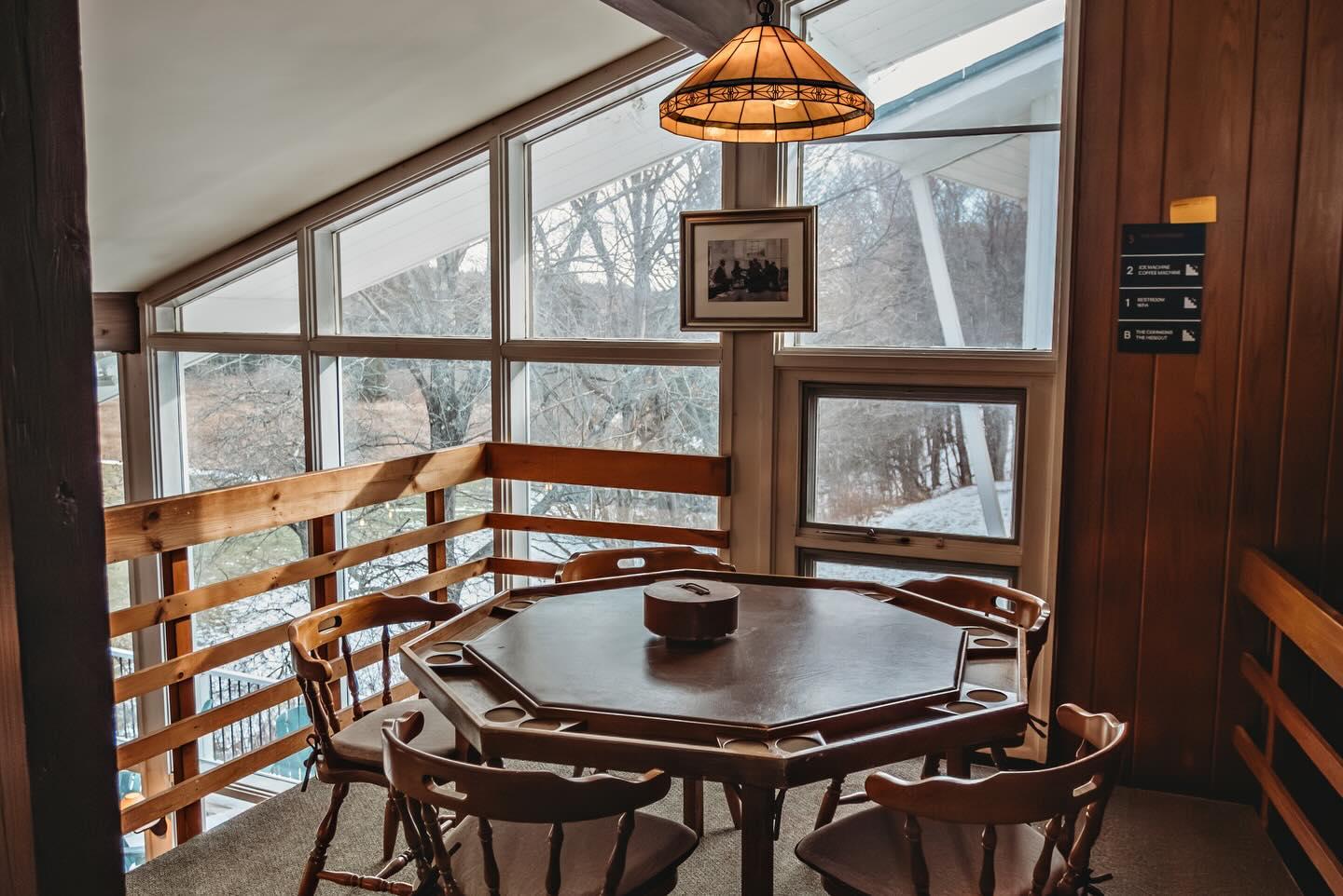 Cozy dining area with wooden table, chairs, large windows, and hanging light.