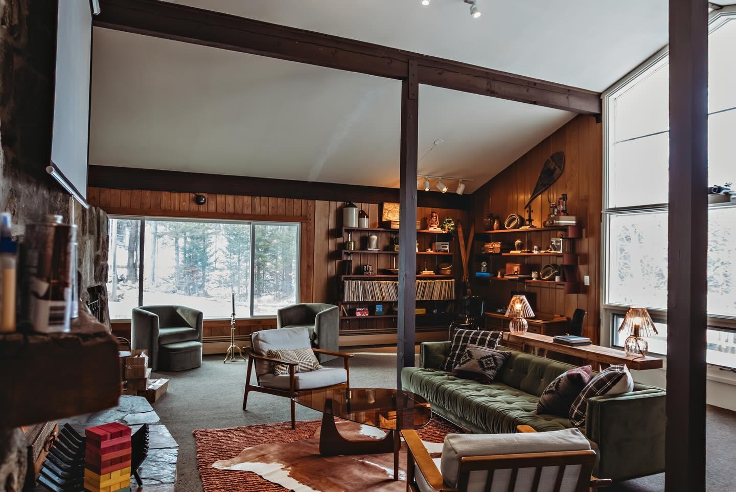Cozy living room with large windows, shelves, sofas, and a warm color palette.