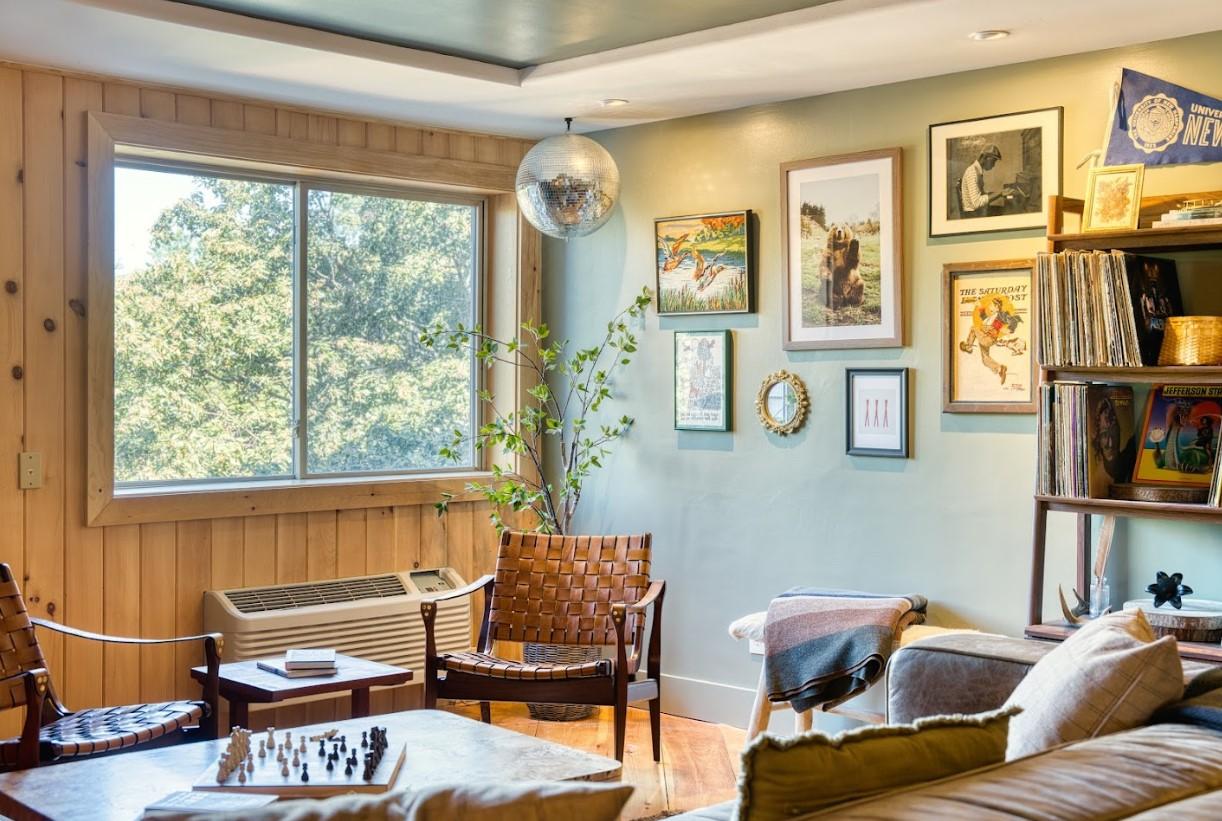 Cozy living room with art, books, and a disco ball, sunlit through a large window.