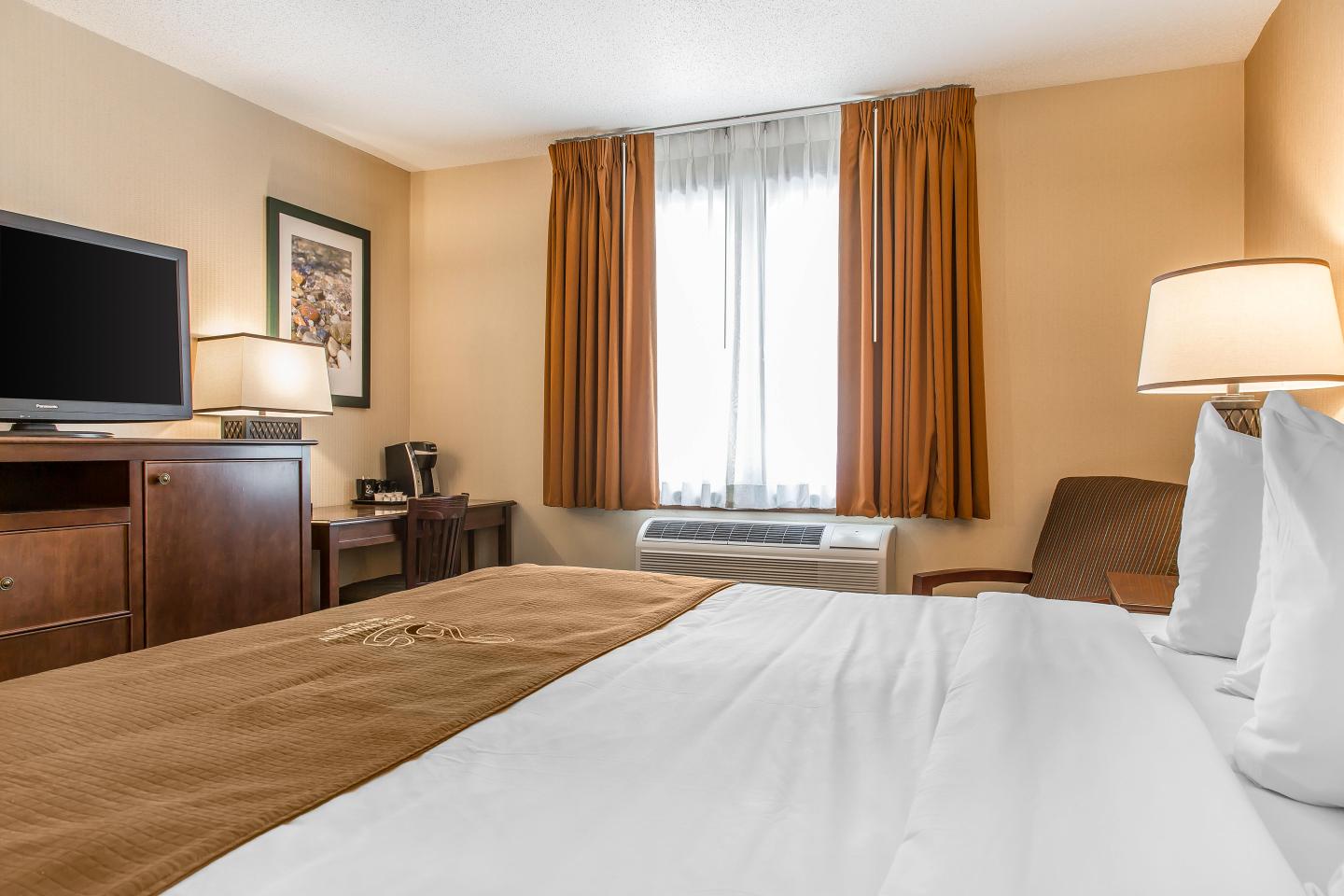 Cozy hotel room with a large bed, TV, and a window with brown curtains.