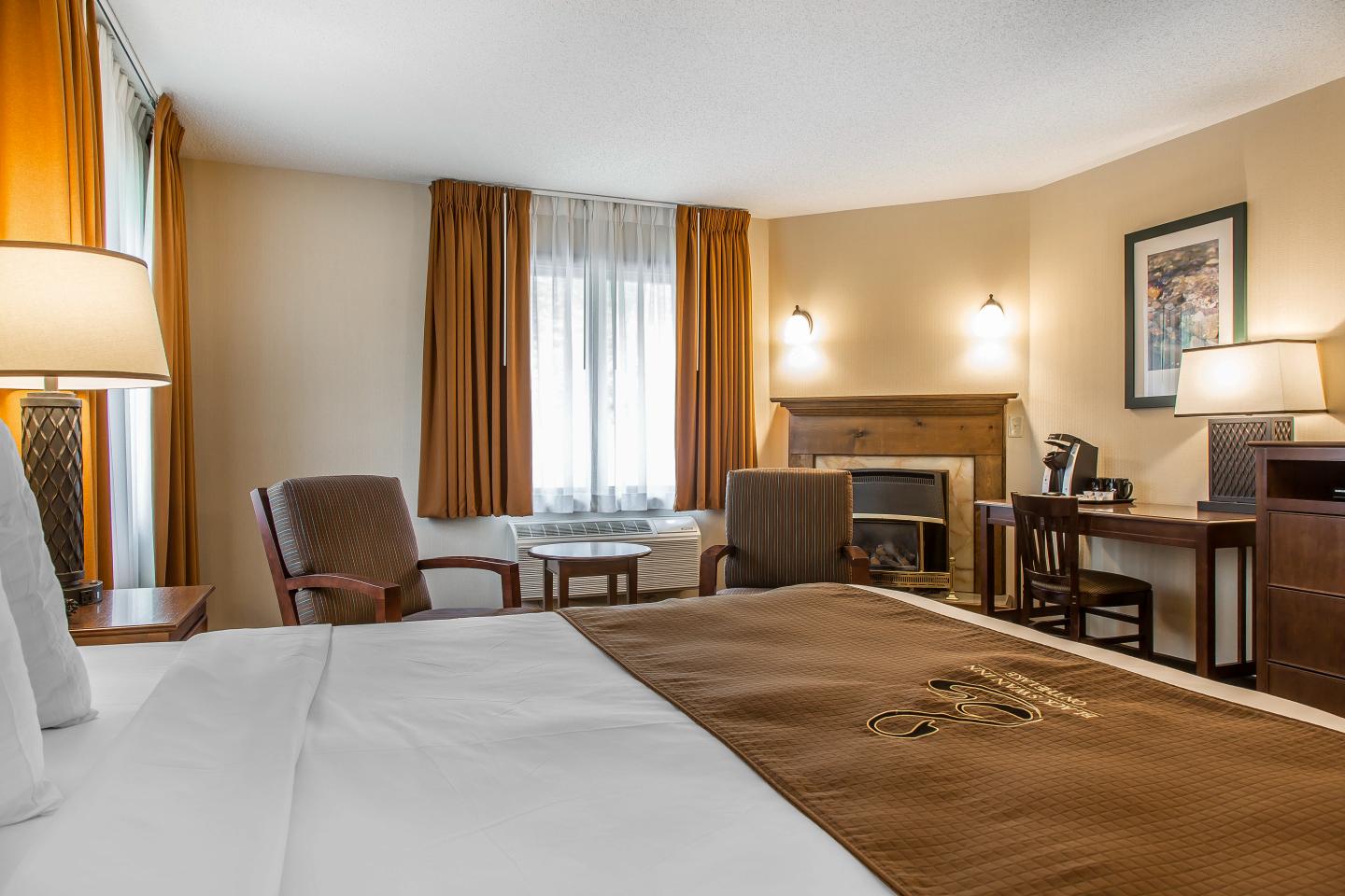 Cozy hotel room with brown bedding, armchairs, and a desk. Warm lighting.