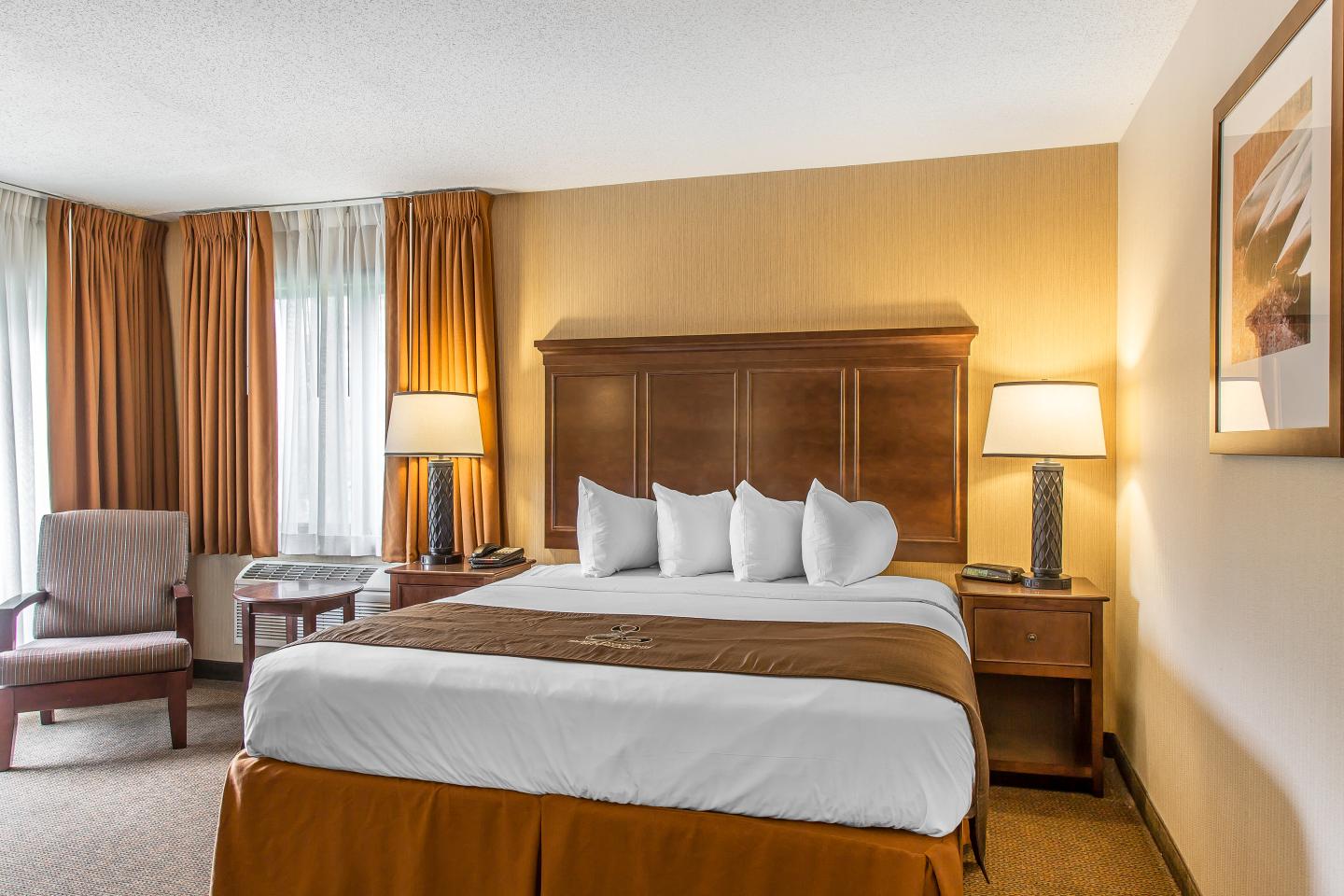 Cozy hotel room with a bed, lamps, and armchair, warm lighting.