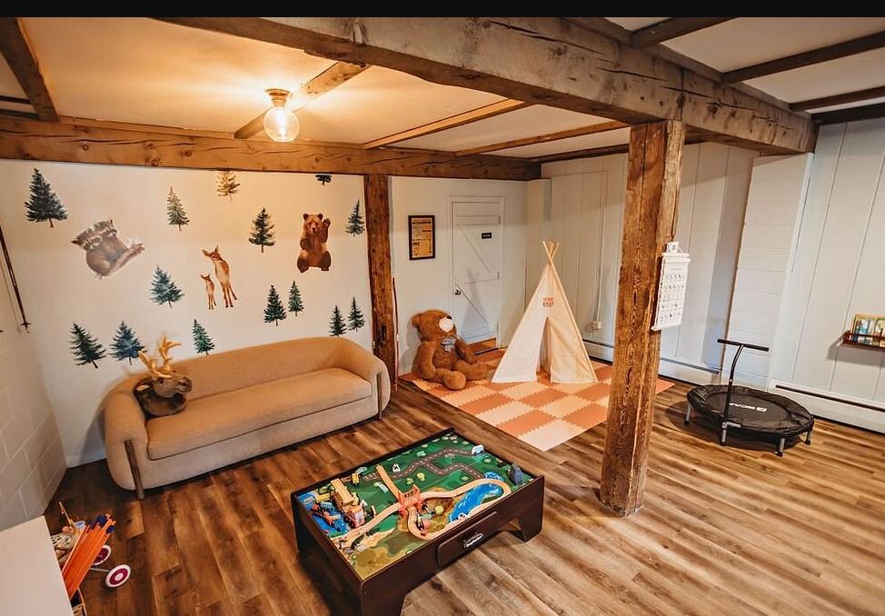 Cozy playroom with wooden beams, a sofa, play table, and teepee tent.