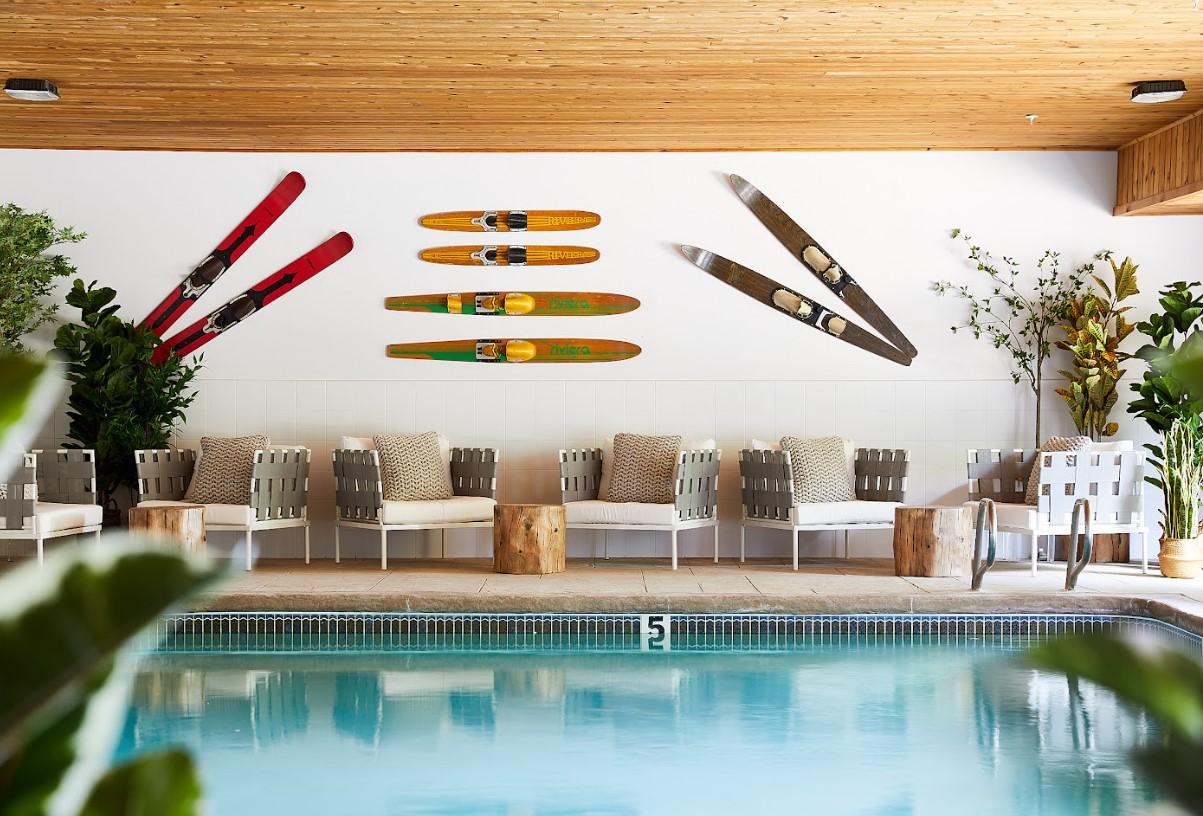 Indoor pool area with surfboards on wall, lounge chairs, and greenery.