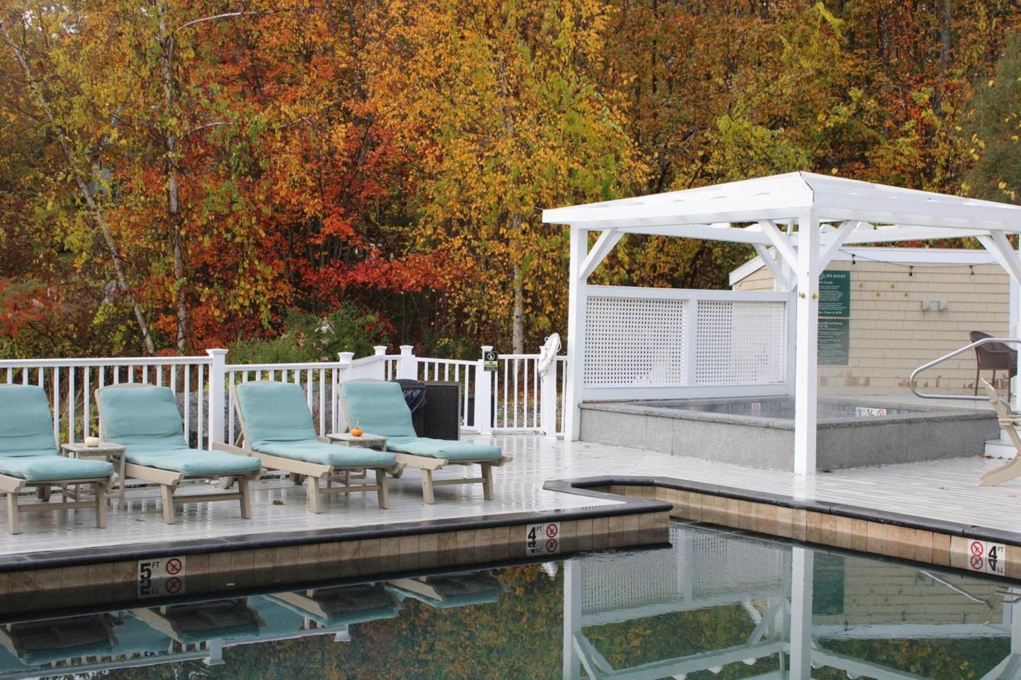Poolside lounge chairs and gazebo with autumn foliage in the background.