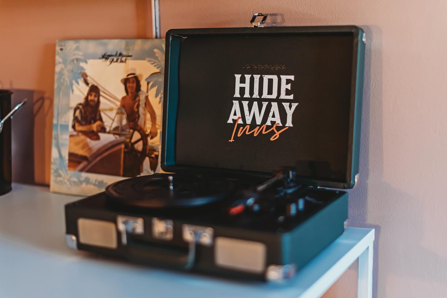 Record player with an open lid on a shelf, album cover in the background.