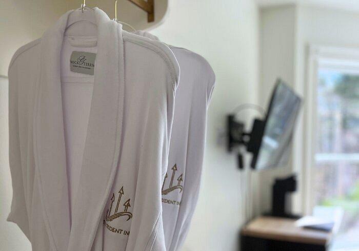 White bathrobes hanging in a bright room with a mounted TV and window.