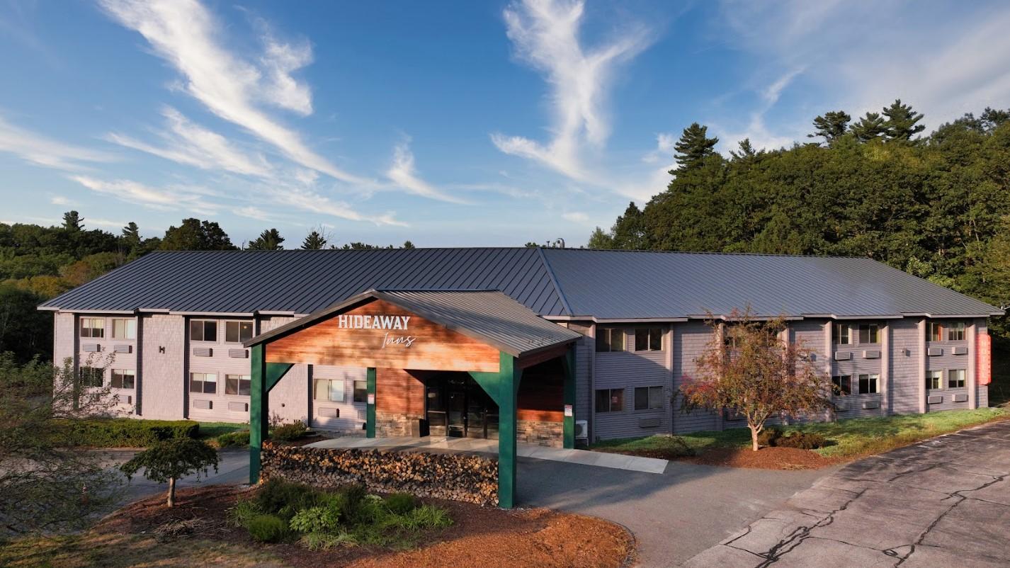Two-story hotel surrounded by trees under a blue sky.