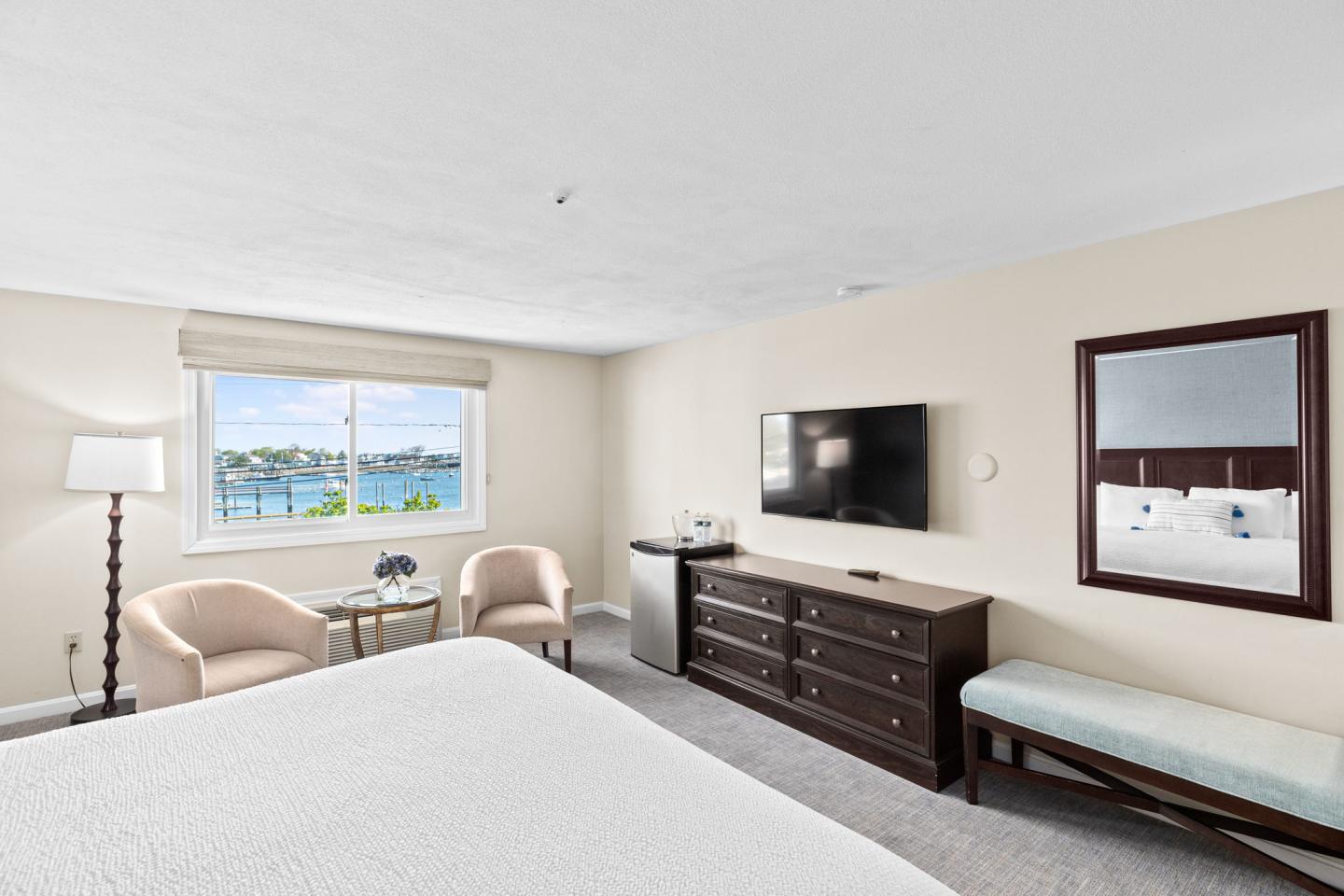 Bright hotel room with bed, TV, armchairs, large window with scenic view.