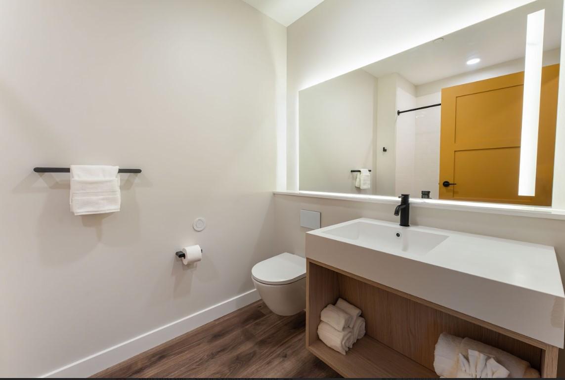 Modern bathroom with large mirror, wooden floor, and white fixtures.