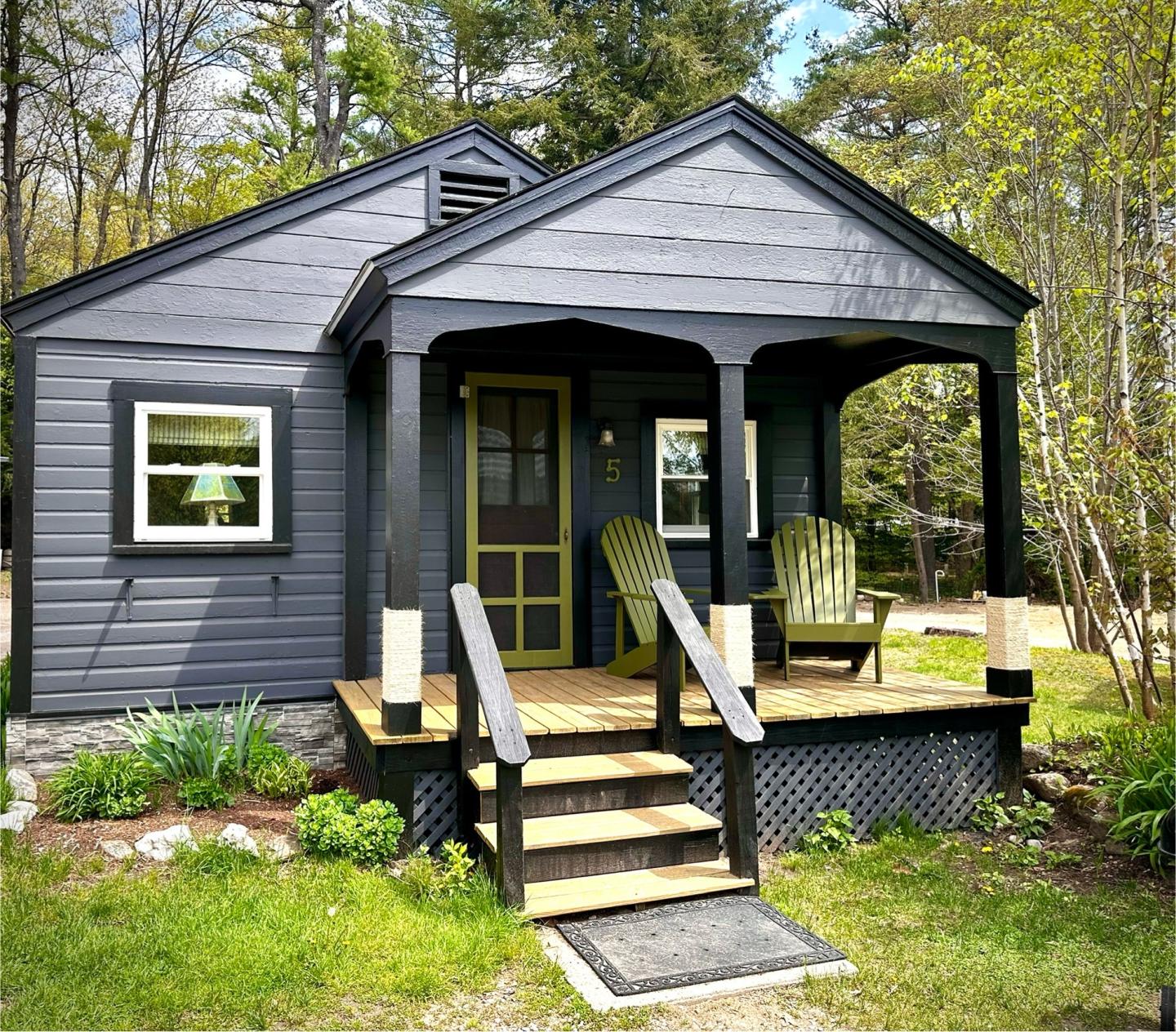 Cozy dark gray cabin with a porch, surrounded by trees.