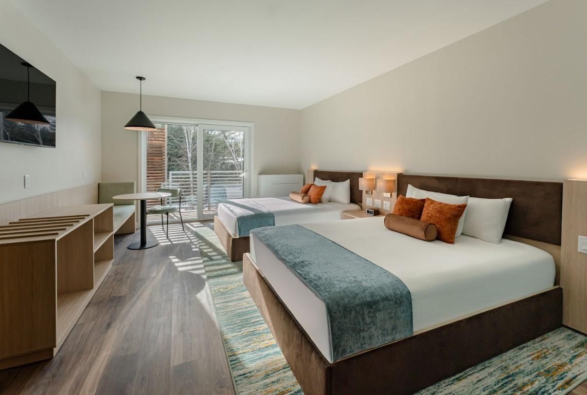 Two neatly made double beds in a modern hotel room with natural light.