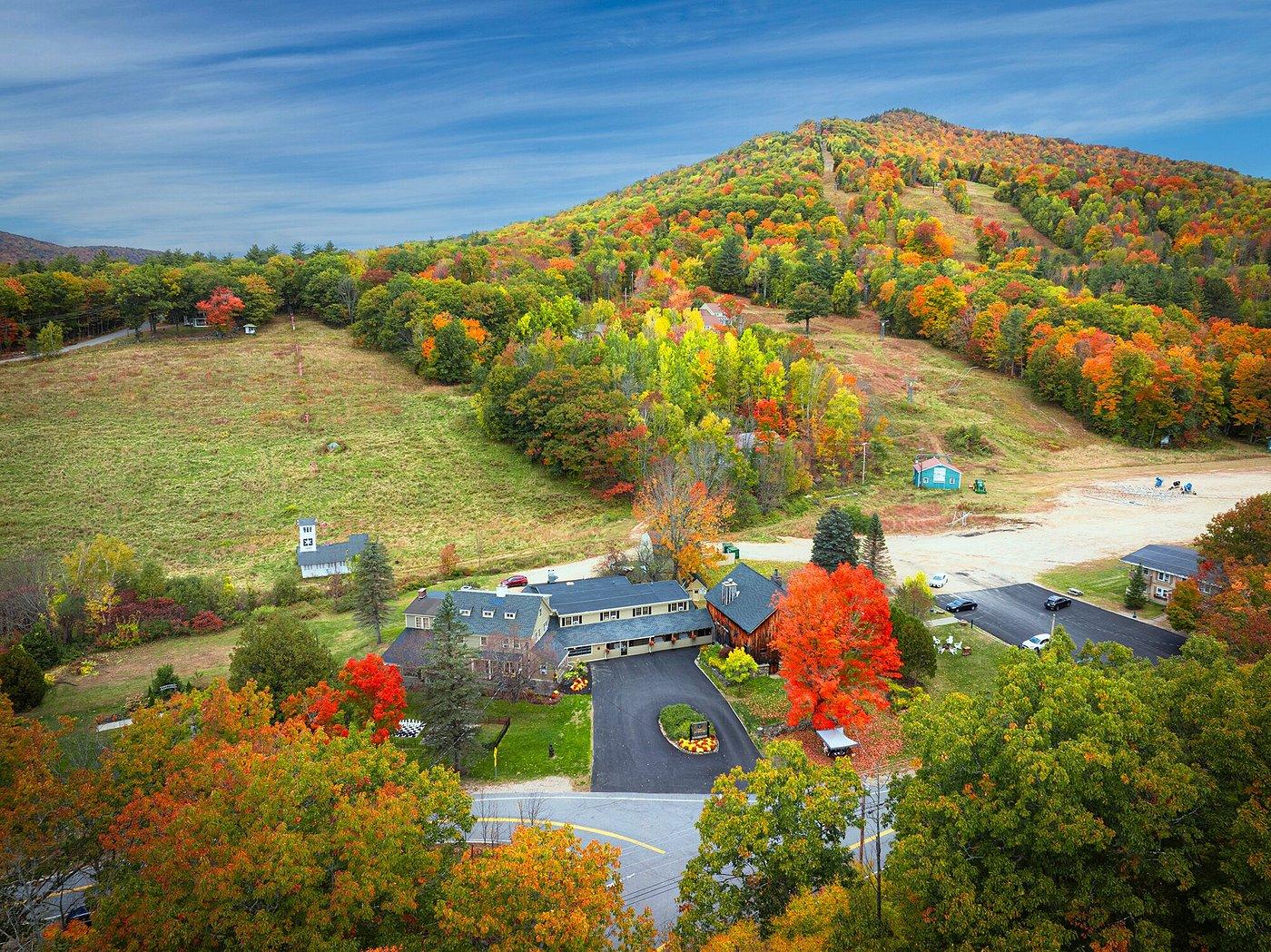 Aerial view of a building surrounded by vibrant fall foliage and hills.