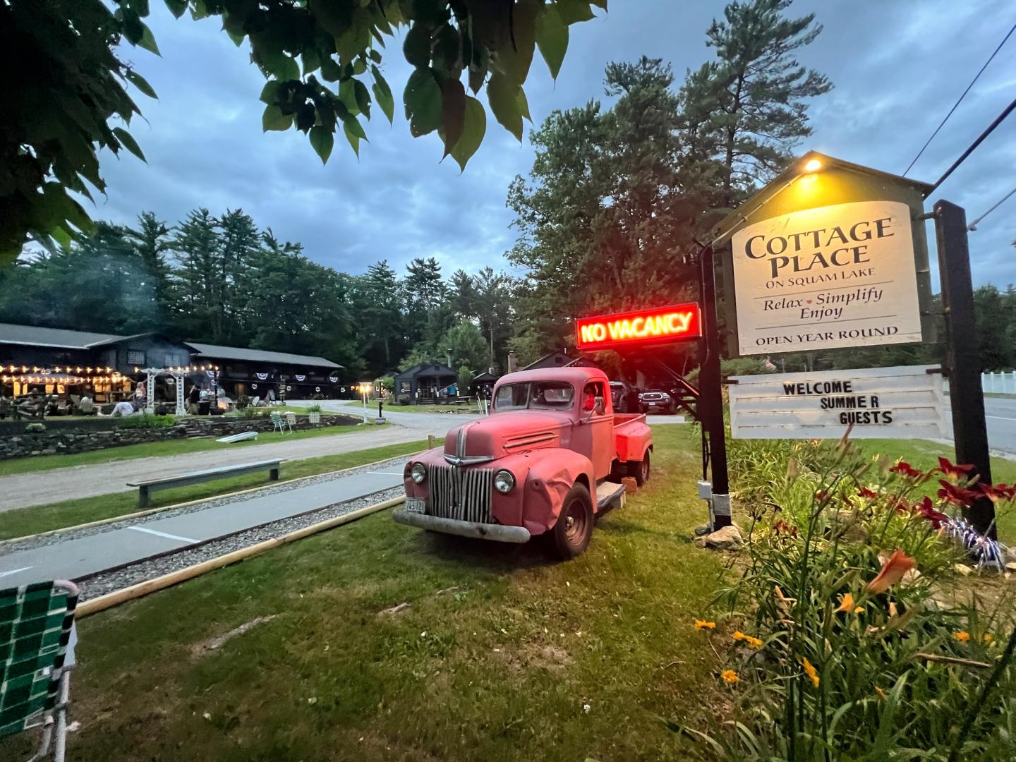 Red vintage truck next to a cottage sign at dusk.