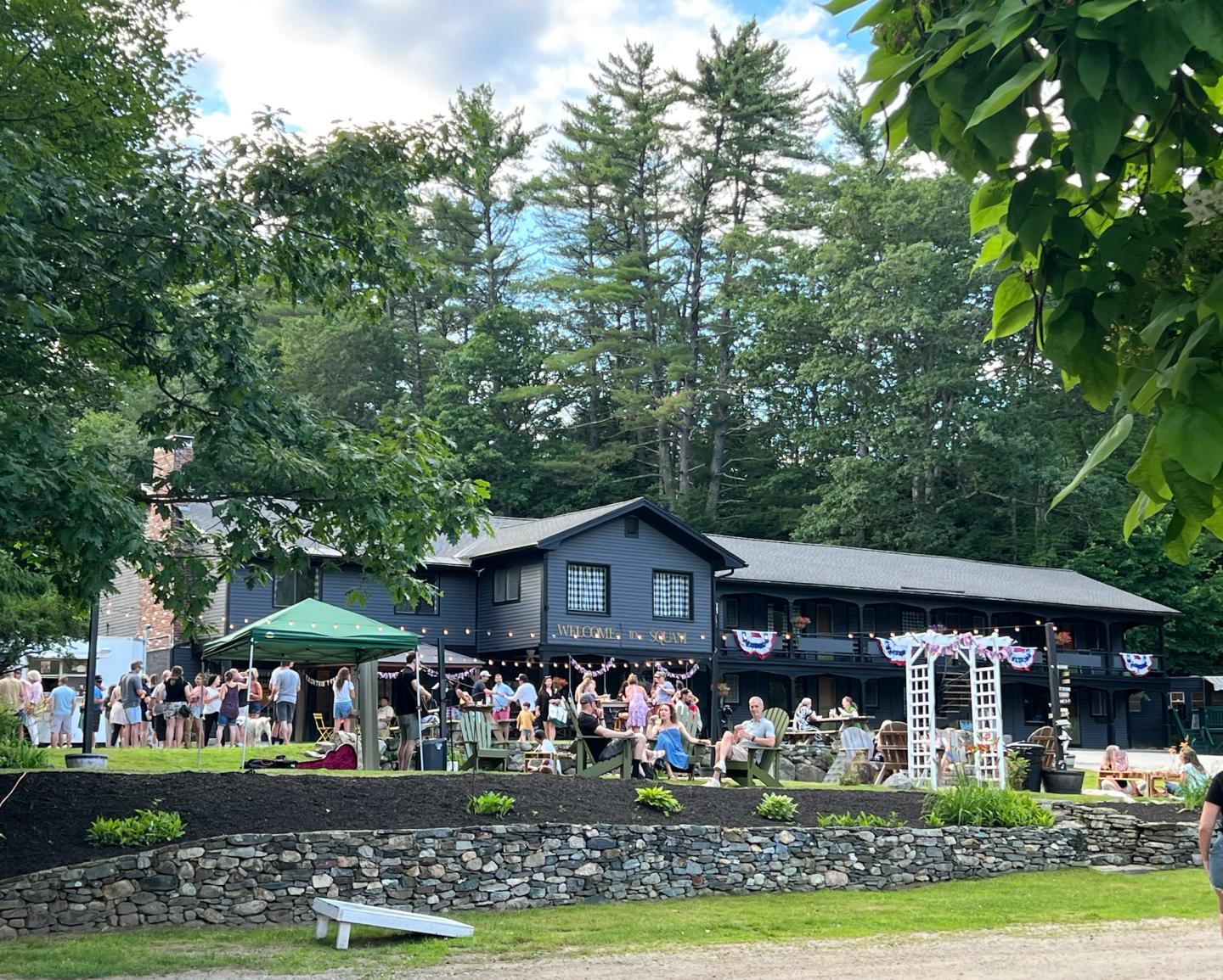 Large group gathering at a lodge with trees and blue sky.
