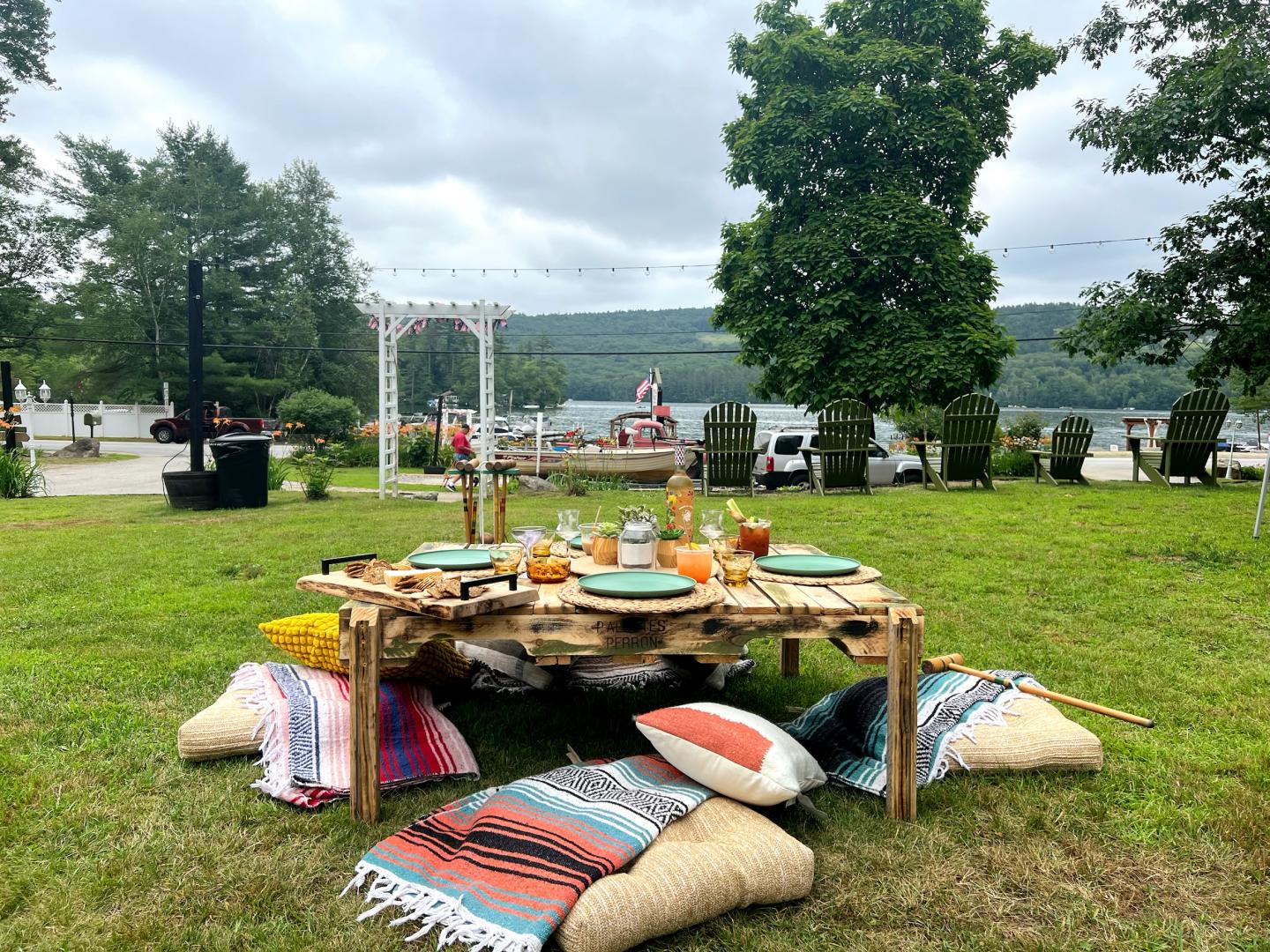 Outdoor picnic setup with a low table, cushions, and a lake view.