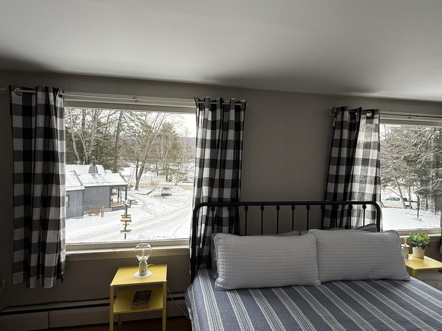 Cozy bedroom with plaid curtains, a striped bed, and snowy outdoor view.