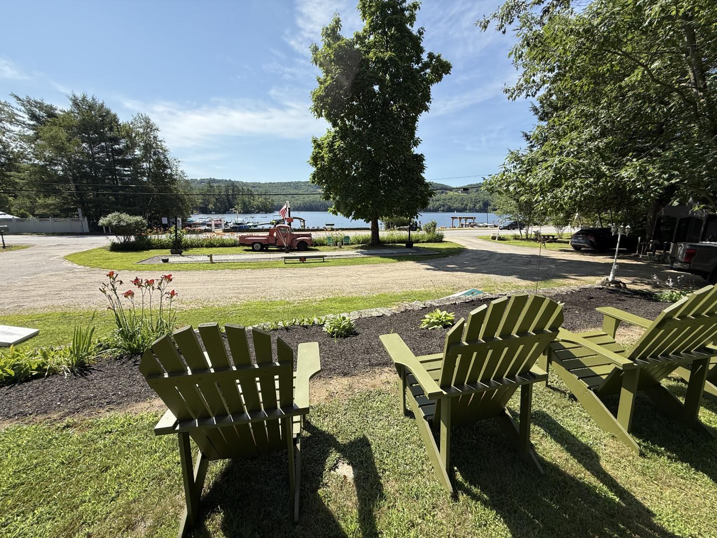 Adirondack chairs facing a lake under a sunny sky.