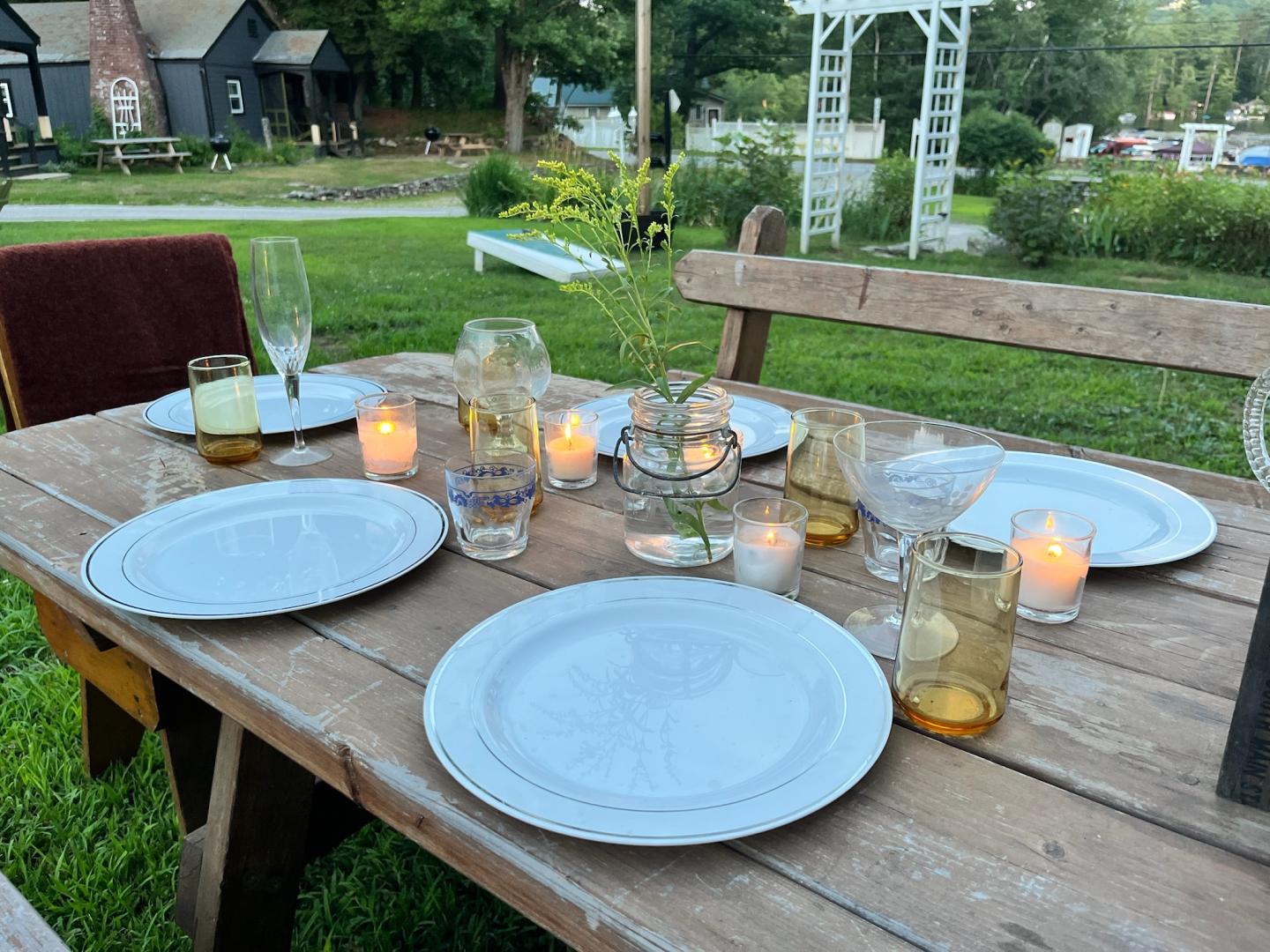 Outdoor dining table set with plates, glasses, and candles on a wooden table.