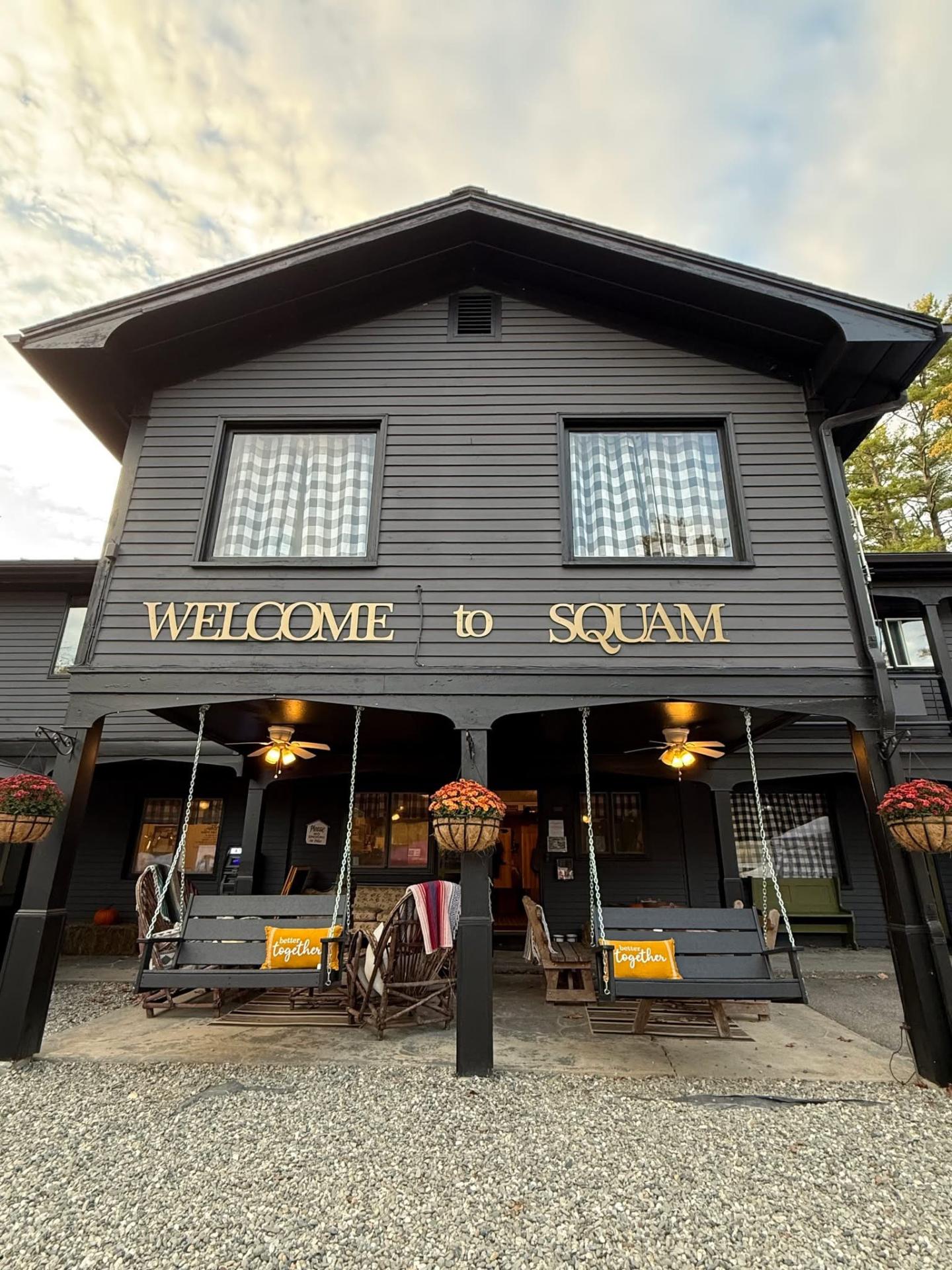 Two-story black building with porch chairs and hanging baskets.
