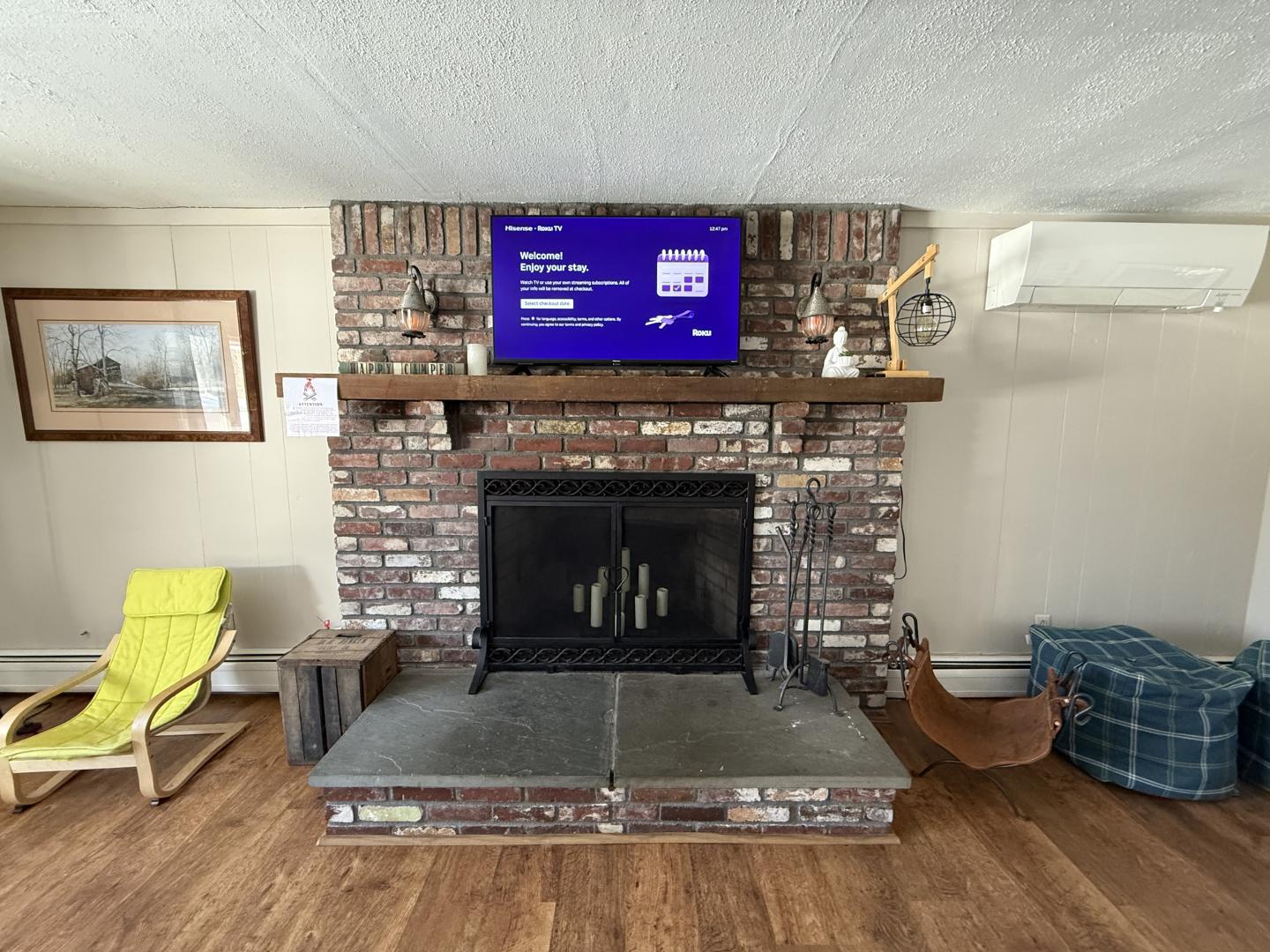 Brick fireplace with TV above, wooden floor, chairs, and wall art.