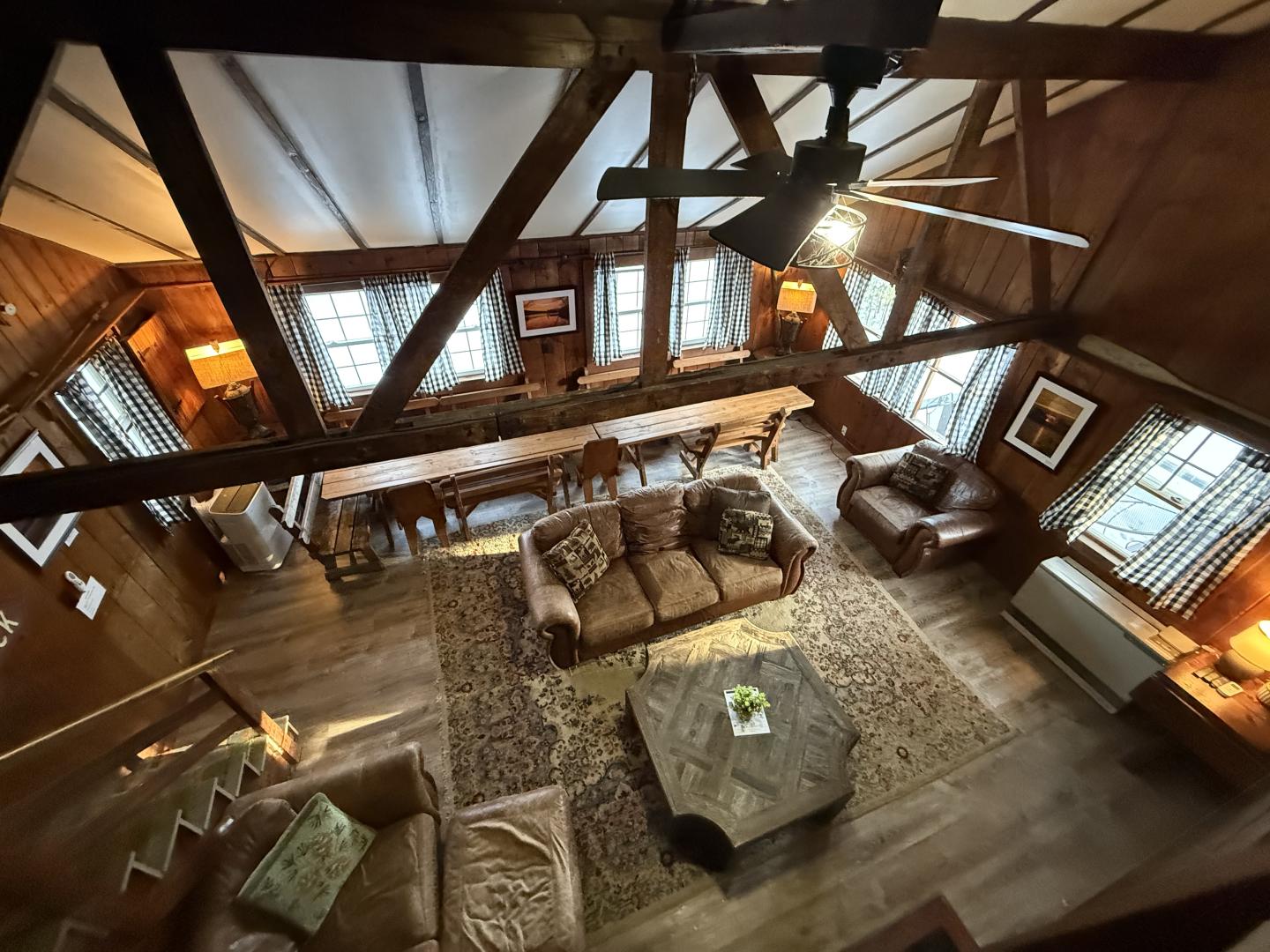 Cozy wooden living room with sofas, large windows, and a dining table.