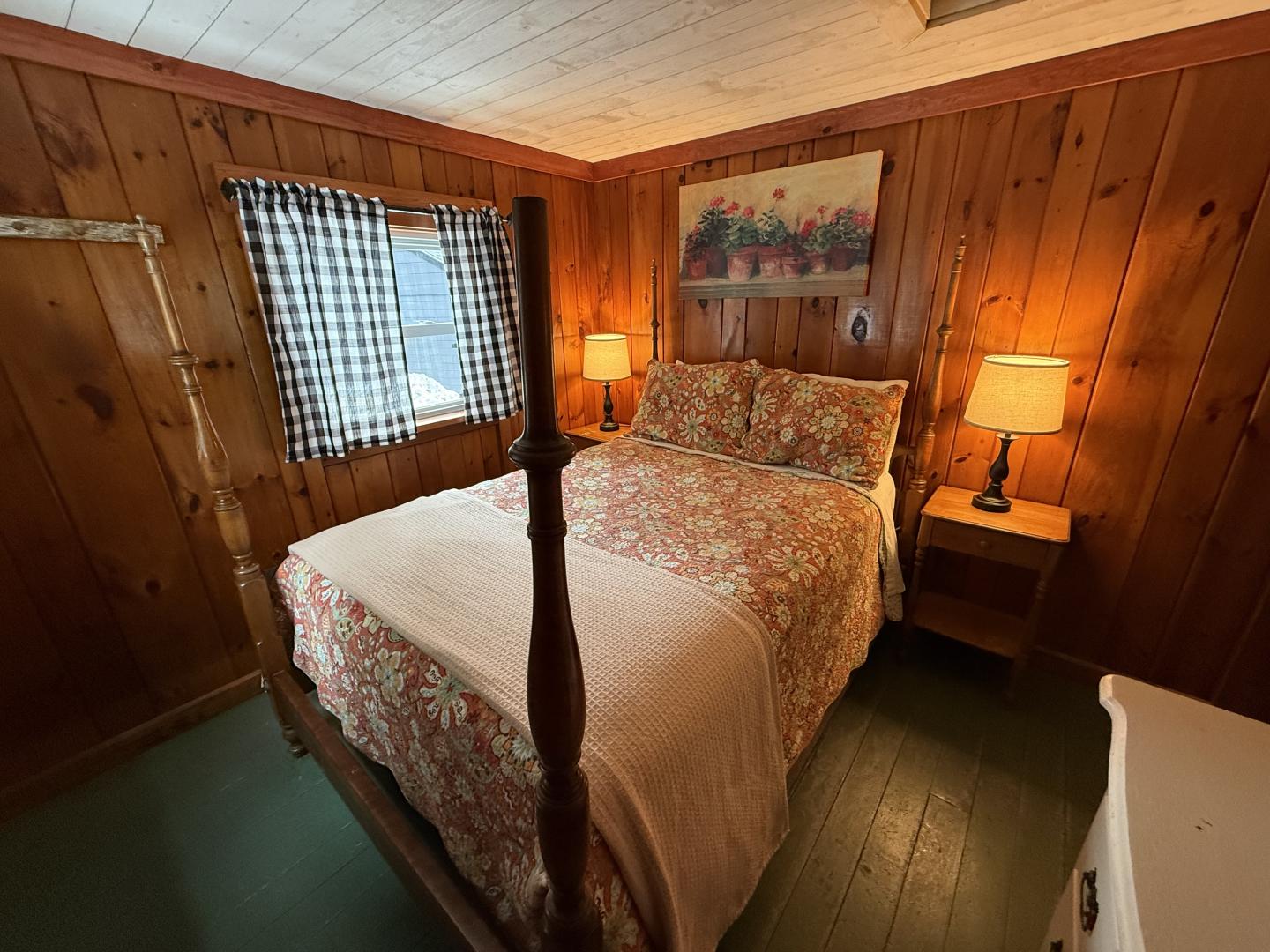Cozy wood-paneled bedroom with a patterned bedspread, lamps, and a painting above the bed.