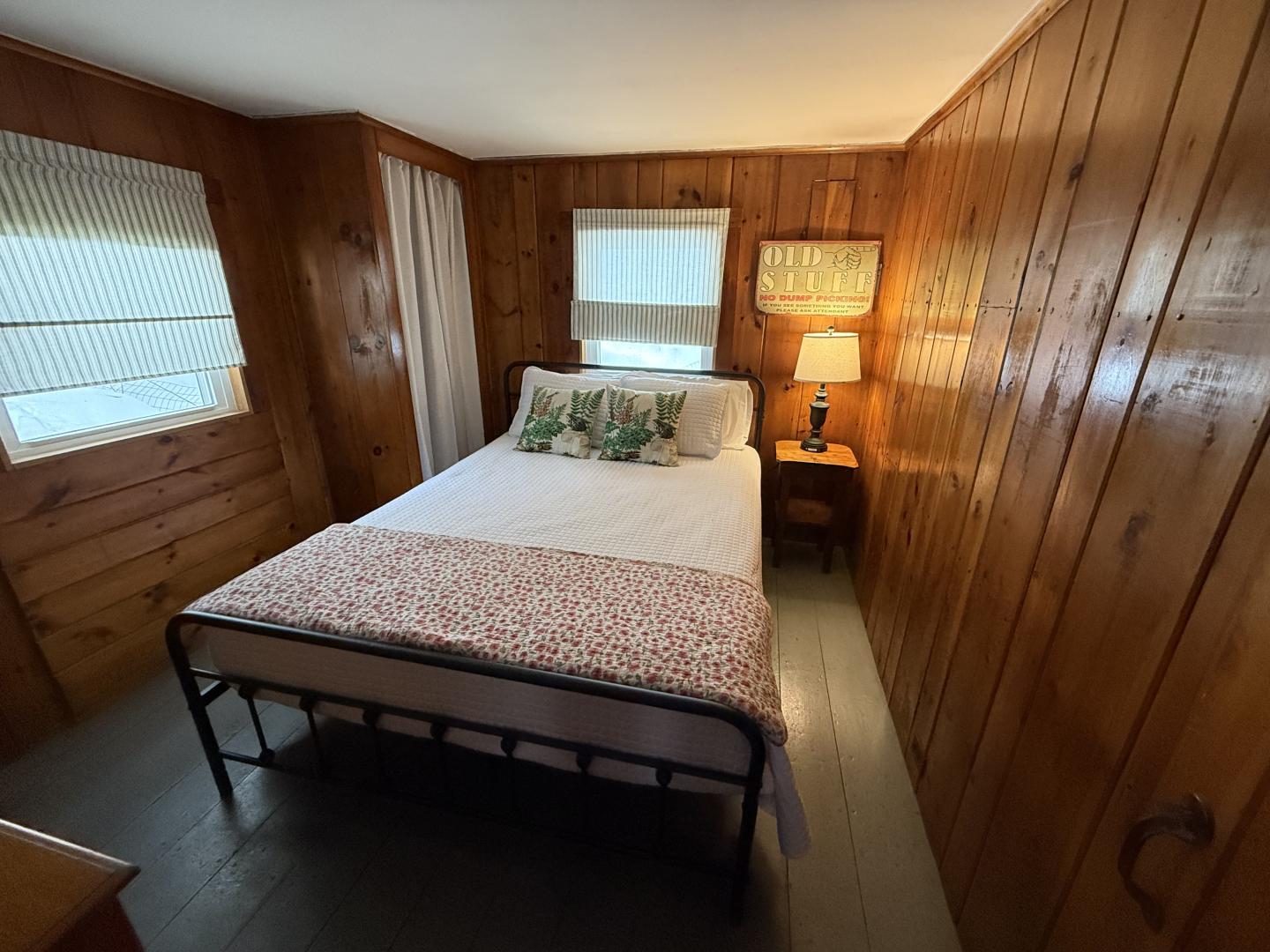 Cozy bedroom with wooden walls, a double bed, and a lit lamp on a side table.