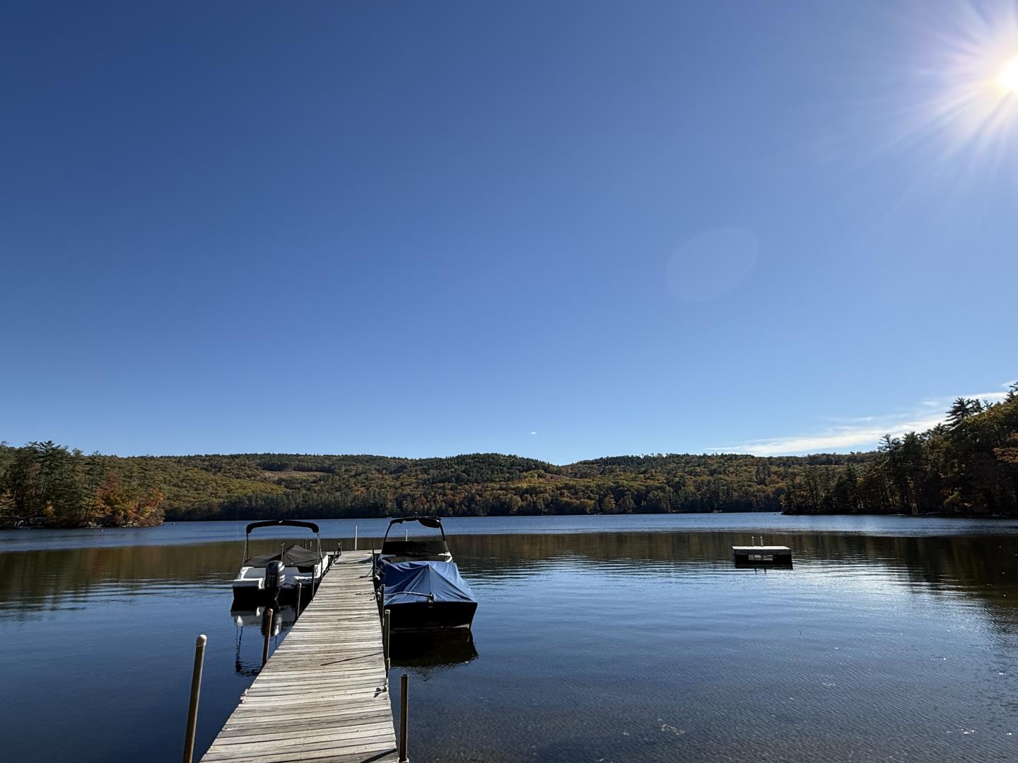 Dock extending into a calm lake under a clear blue sky with distant hills.