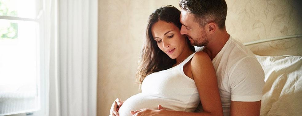 Couple embracing, woman pregnant, sitting near window in soft light.