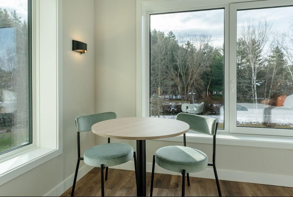 Cozy dining area with round table, two chairs, large windows; wintery view outside.