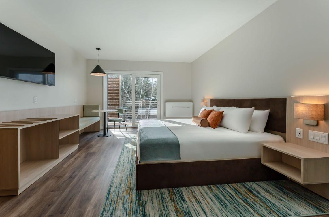 Modern hotel room with a large bed, wall-mounted TV, and a view of an outdoor patio.