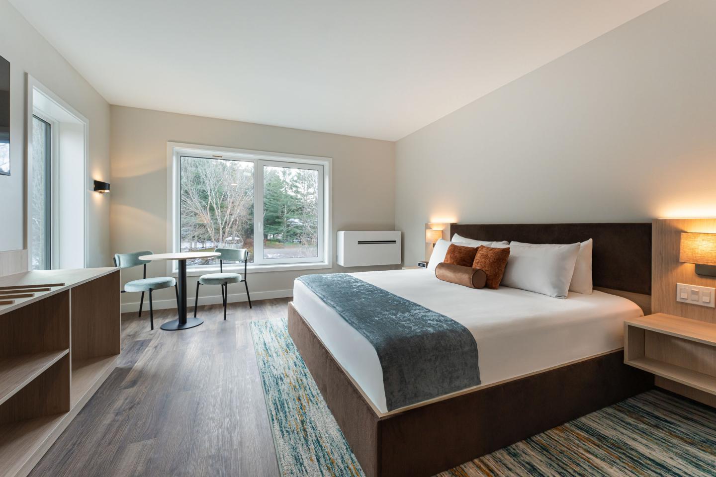 Modern hotel room with a large bed, window, and a small table with chairs.