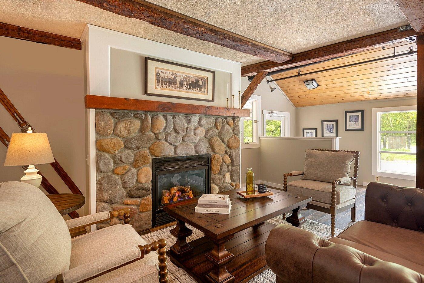 Cozy living room with stone fireplace, wooden beams, and seating arrangement.