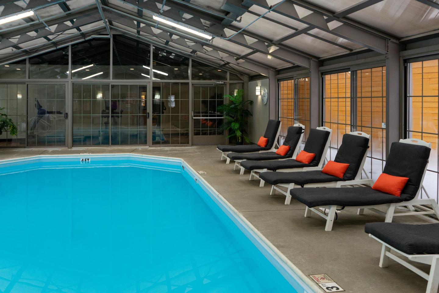 Indoor pool with lounge chairs and orange cushions under a glass roof.