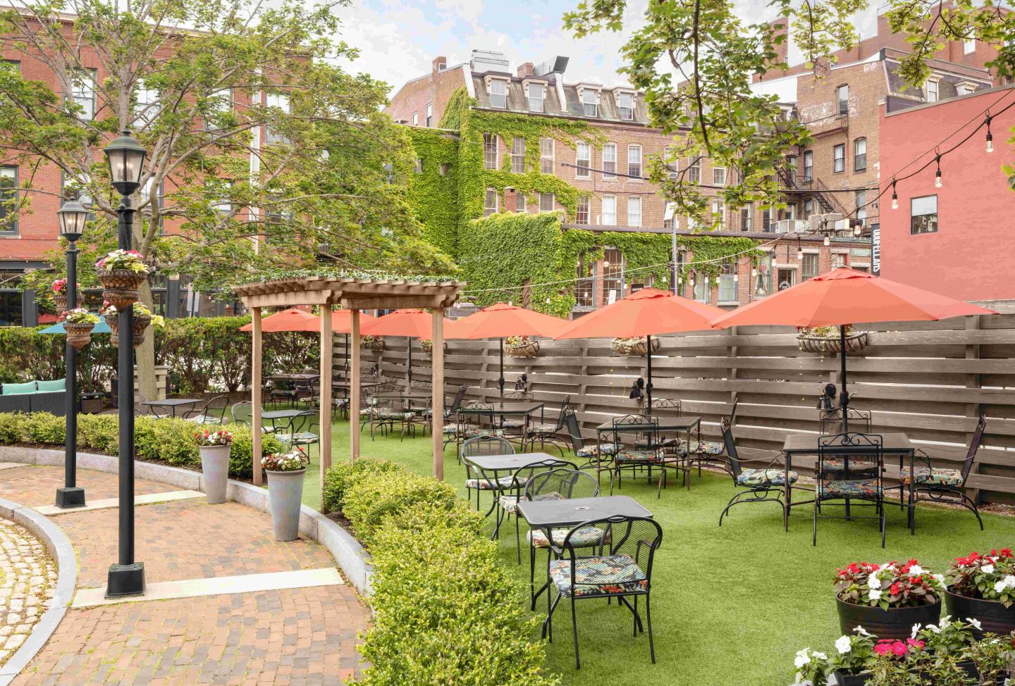 Outdoor patio with orange umbrellas, metal tables, chairs, and lush greenery.