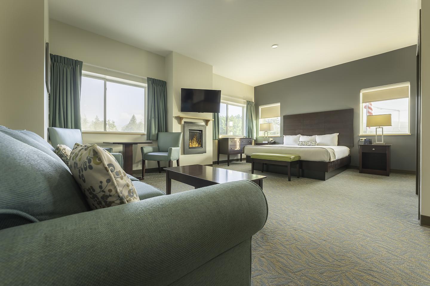 Spacious hotel room with a bed, sofa, and fireplace.