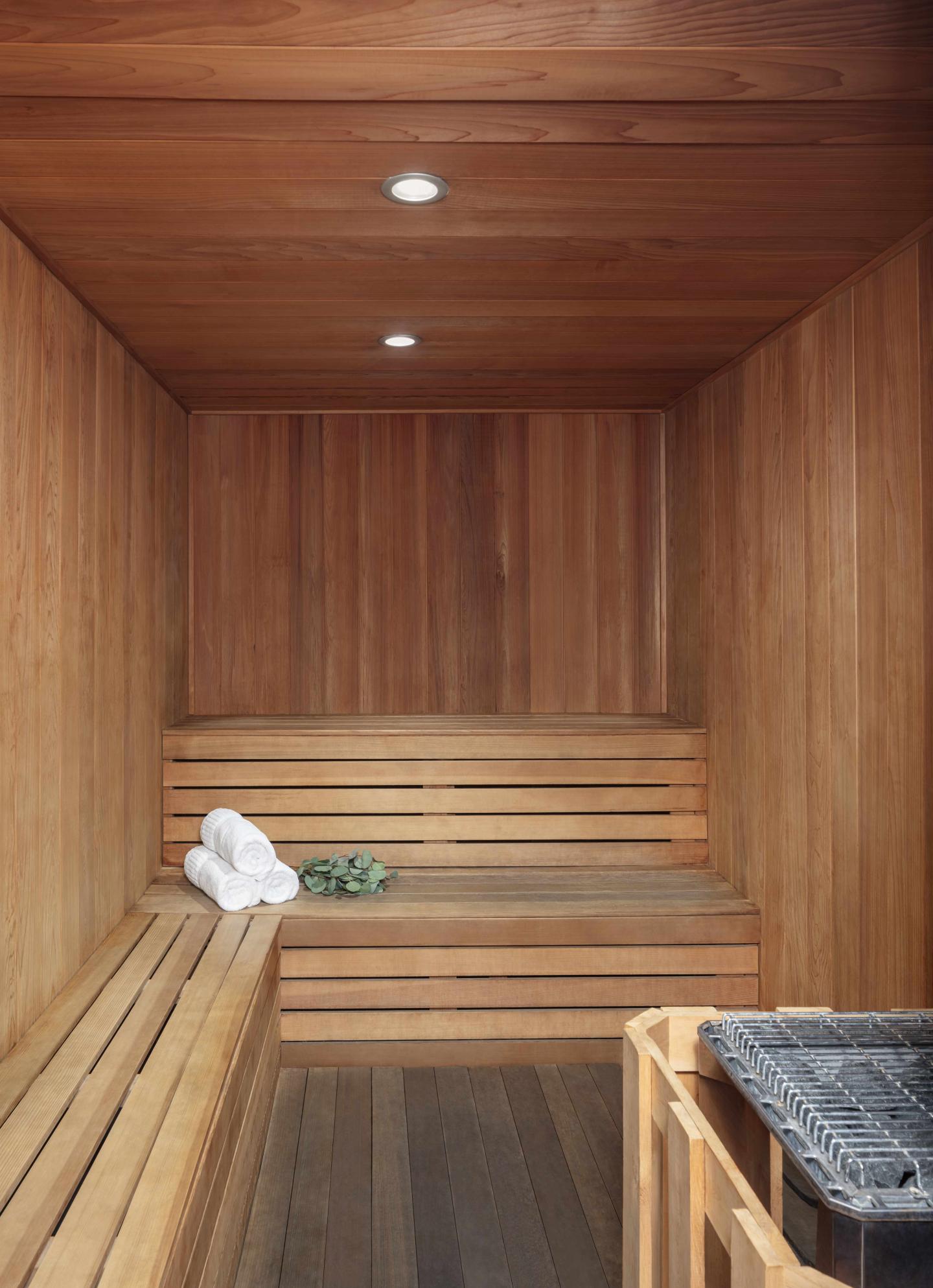 Wooden sauna interior with benches, folded towels, and small plant.