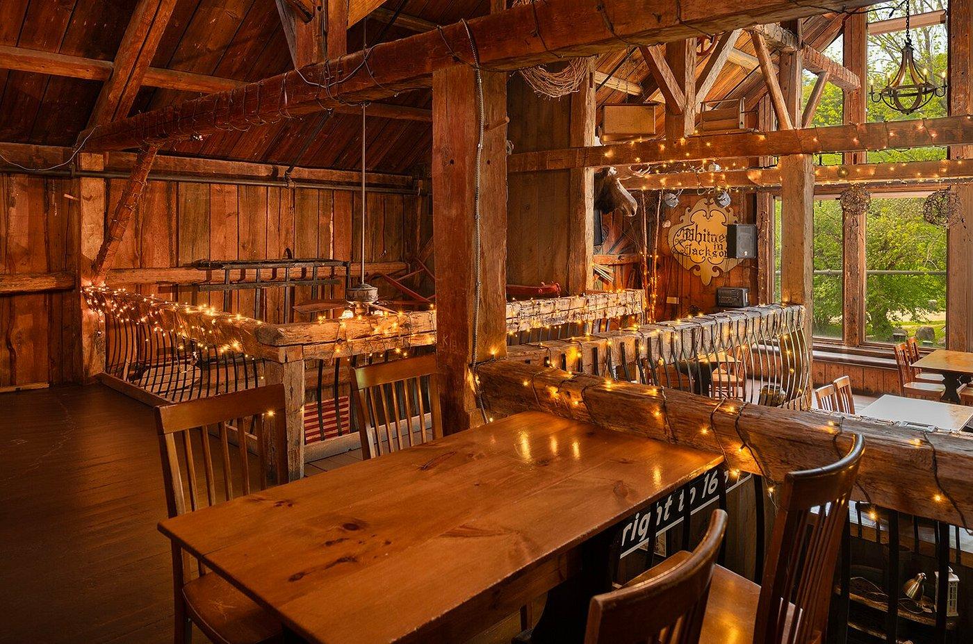 Rustic wooden dining room with string lights, empty tables, and large windows.