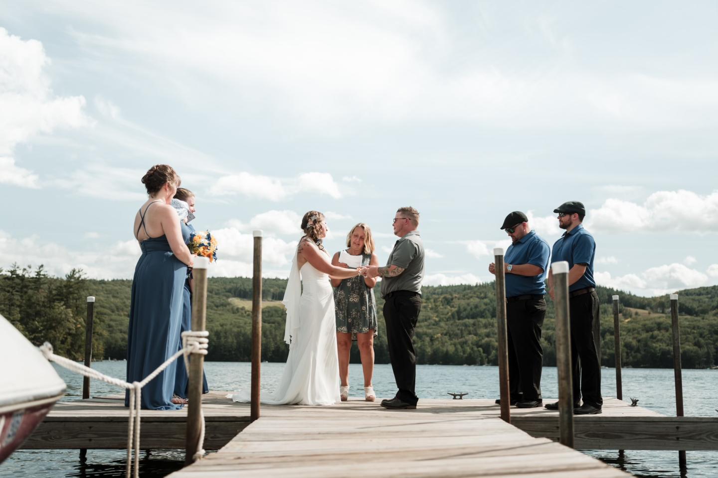 Wedding ceremony on a dock by a lake, with mountains in the background.