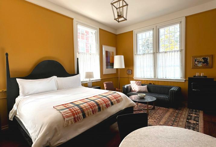 Cozy bedroom with mustard walls, large bed, sofa, and natural light from windows.