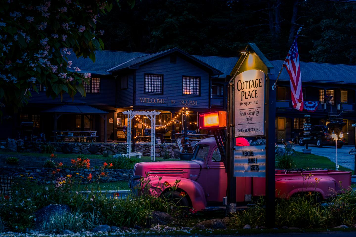 Pink vintage truck and illuminated sign, cozy lodge in evening light.