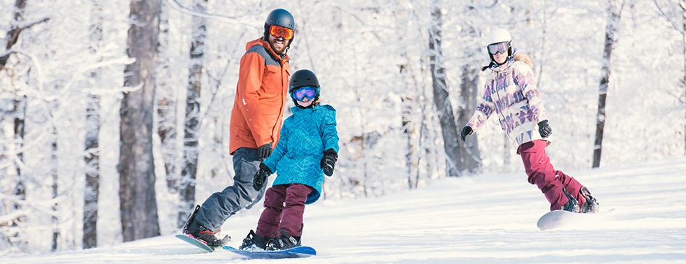 Snowboarders on a snowy slope, surrounded by trees.