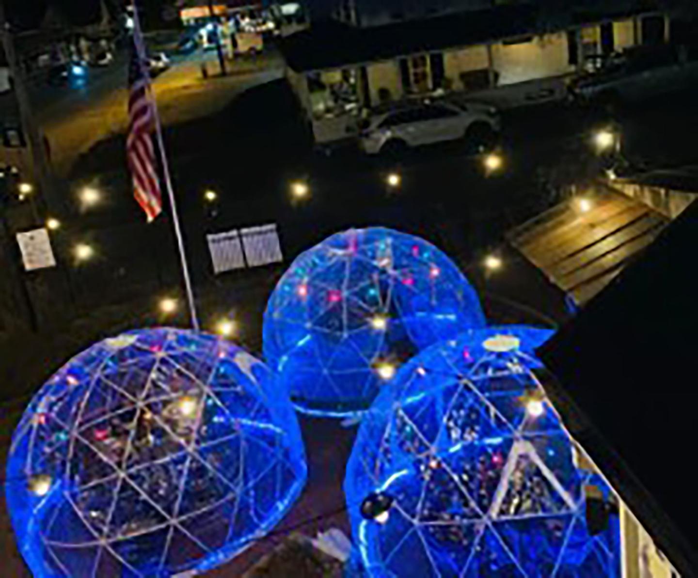 Three glowing blue igloo-shaped tents on a nighttime patio.
