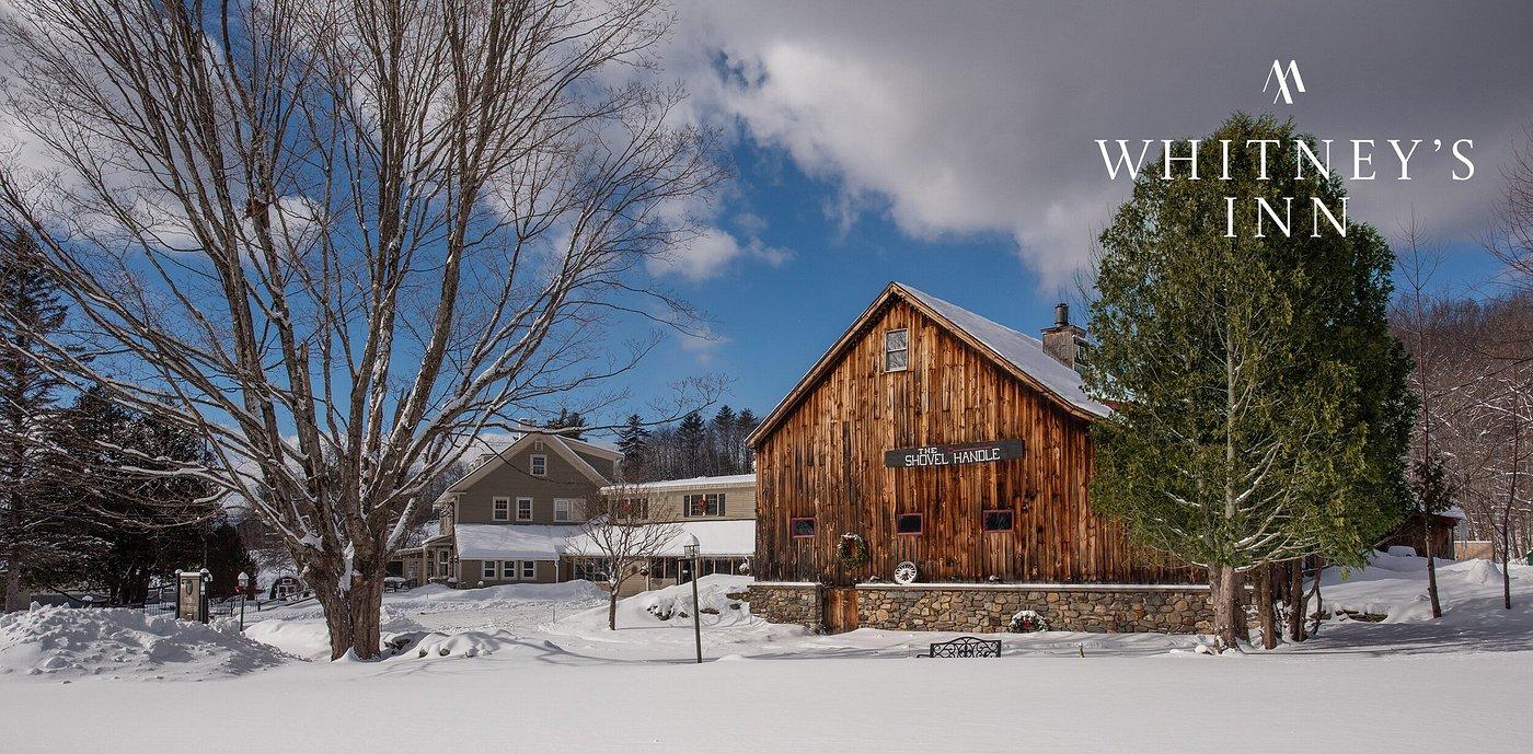 Historic wooden barn in snowy landscape with evergreen trees and a clear blue sky.