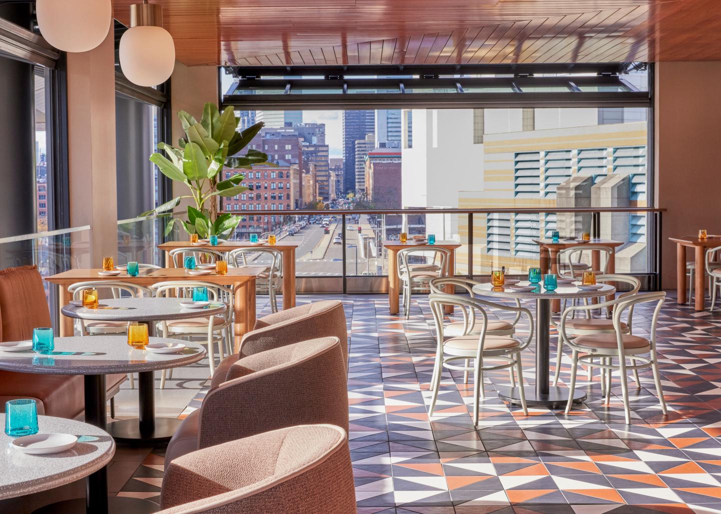 Bright, modern restaurant with city view, colorful glassware, and geometric flooring.