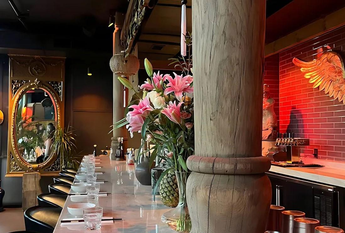 Restaurant bar with flowers, decorative mirror, and red brick wall with golden wings.