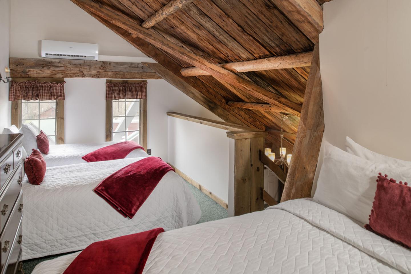 Cozy attic bedroom with two beds, red pillows, and wooden beams.