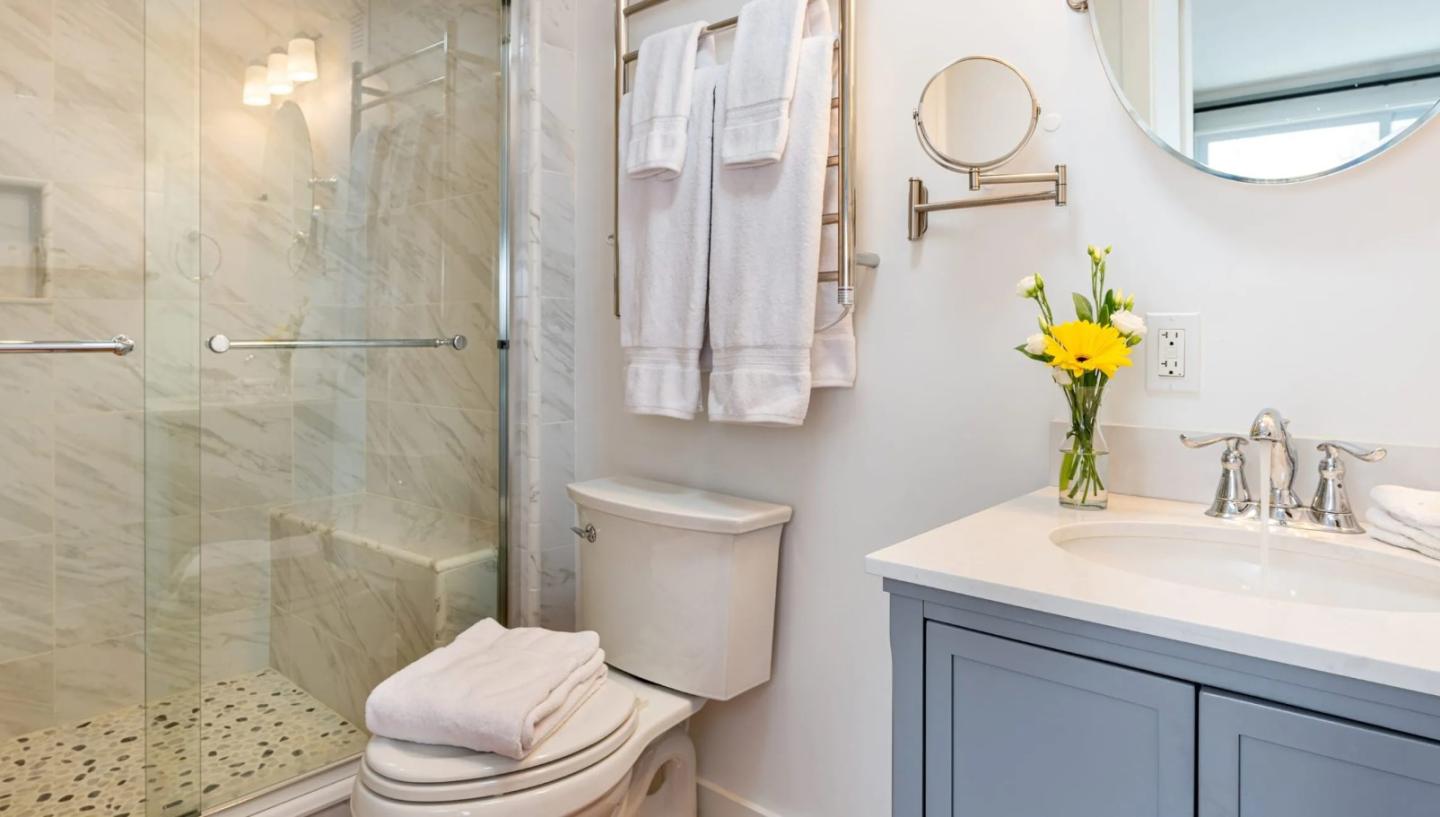 Modern bathroom with a glass shower, white towels, and yellow flowers on the sink.