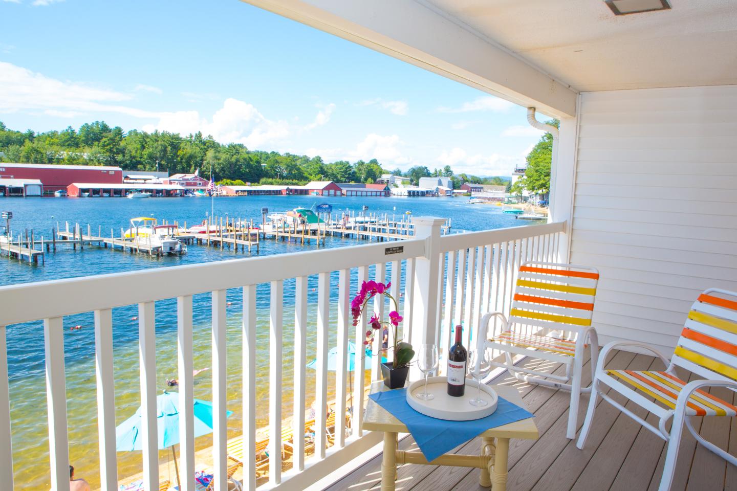 Balcony with chairs overlooking a boat docks and a flower on a table.